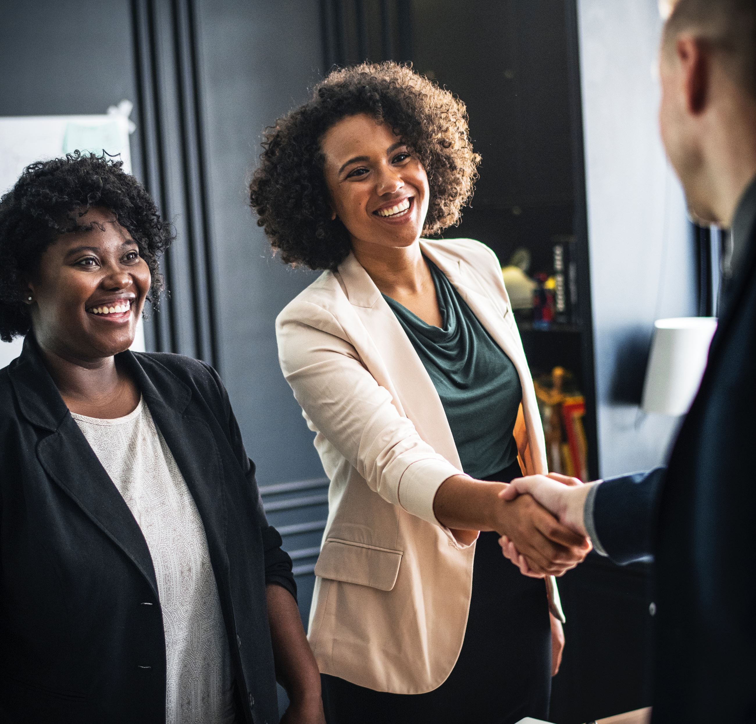 Professional woman with a female colleague shakes man's hand in a business deal 